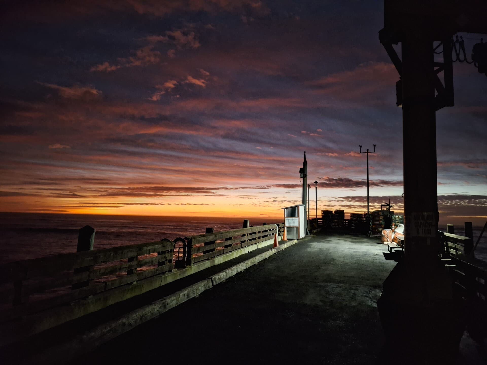 A pier walkway under a dramatic pink and orange twilight sky
