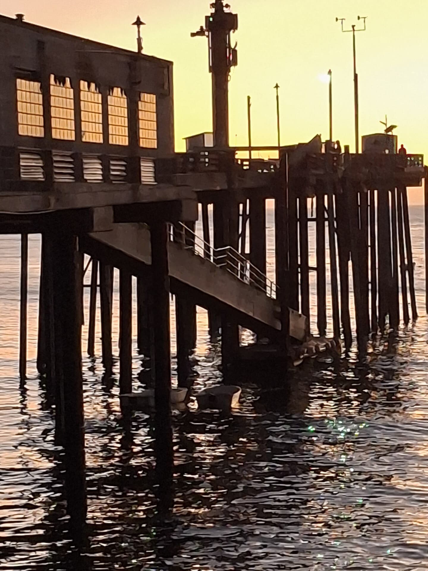 A wharf and pier structure silhouetted against a golden sunset over the water